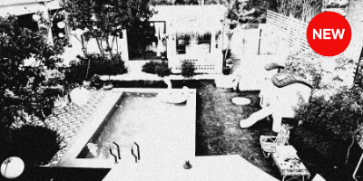 A high-contrast black and white photograph of a children's playground in winter. The playground equipment, including slides and climbing structures, stands starkly against a snow-covered ground. The image has a grainy, dramatic quality typical of Moriyama-style photography, with strong blacks and whites creating a stark, almost abstract composition. Trees and other playground elements frame the scene, emphasizing the emptiness and stillness of the winter playground.